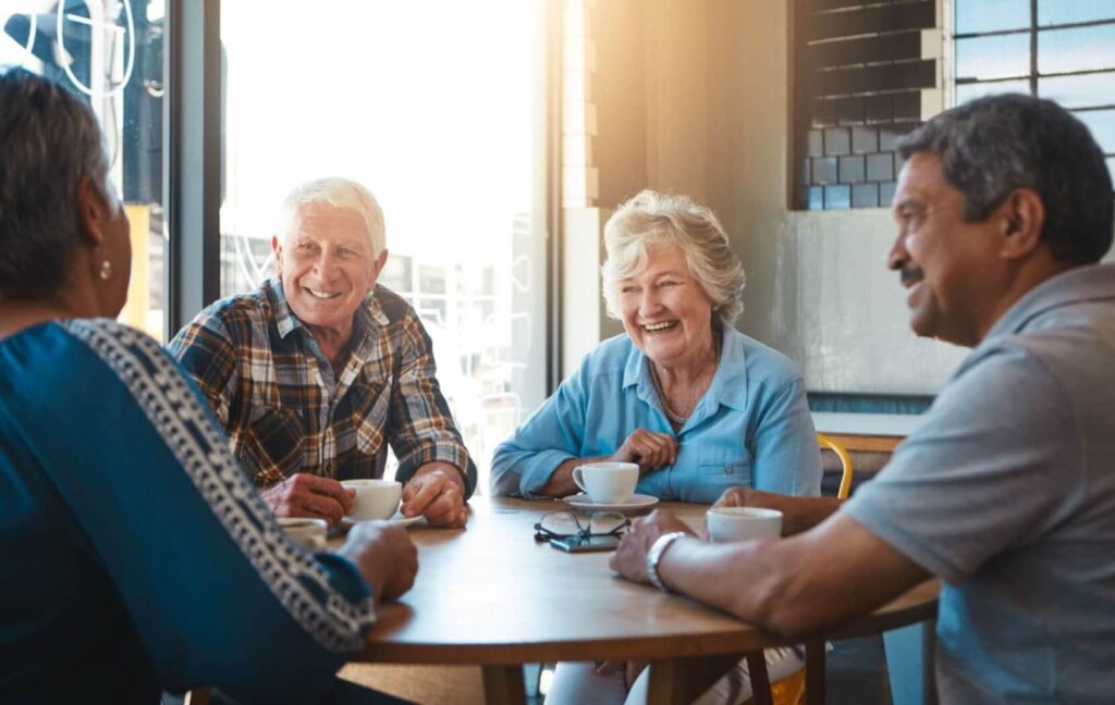 A group of happy seniors laugh and share coffee in a communal space after attending a fun trivia activity.