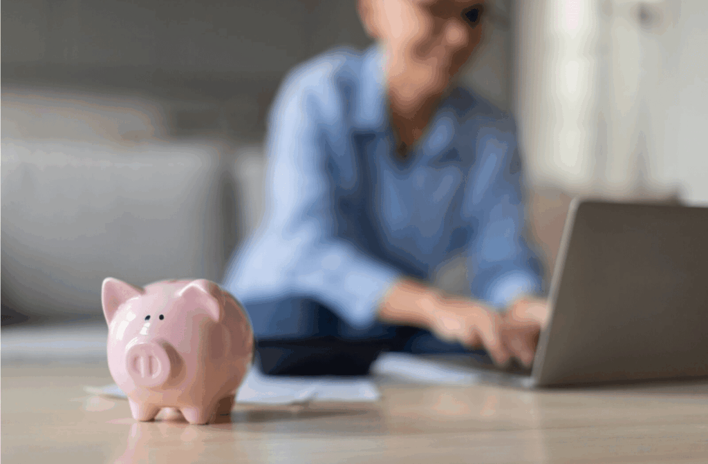 A pink piggy bank in front of a senior using a laptop to sort through financials to make payment plans for assisted living